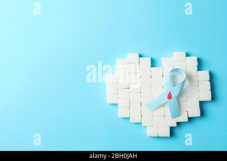 Diabetes awareness ribbon and heart made of sugar cubes on blue background Stock Photo