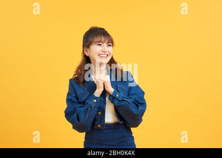 Close up photo of excited cheerful nice glad positive optimistic young lady holding hands together looking at you isolated yellow background