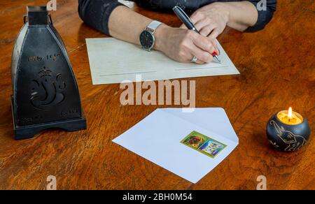 Detail of female hands about to write a letter with pen and paper on an old wooden table with burning candle and black lantern Stock Photo
