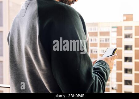 unrecognizable man checking his smart phone on the balcony of his house, concept of communication and work from home Stock Photo