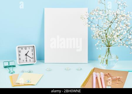 Mockup with blank white frame on blue table against blue wall, alarm, flower in vaze. Stock Photo