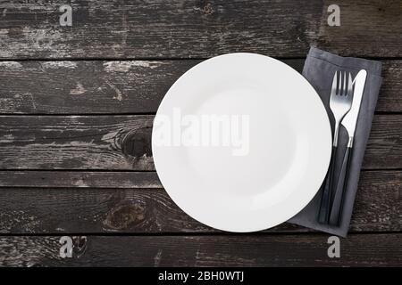 clean empty white plate, fork and knife on gray old rustic wooden table, copy space, mock up Stock Photo