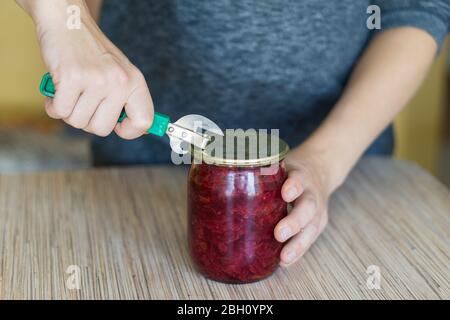 Closeup of woman opening a can in a kitchen with old style tin opener. Stock Photo