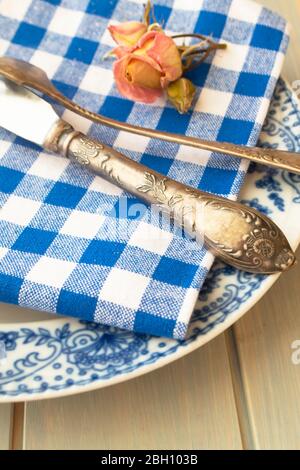 Silver fork and knife with an empty vintage plate on a blue napkin, with dry pink rose Stock Photo