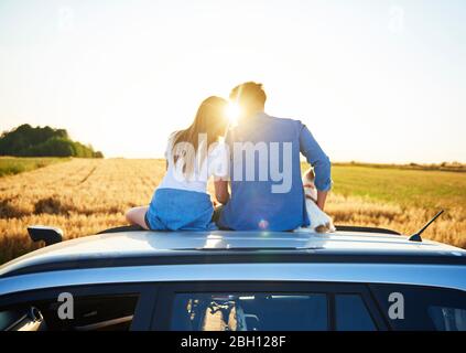 Rear view of loving couple embracing and sitting on car Stock Photo
