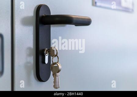 Door lock keys, Real estate concept door handle, Key insert and hold in metallic knob on white door horizontal. Stock Photo