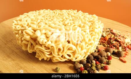 circle of instant noodles with raw spices on a plain brown background. Sprinkle dry Chinese or Korean vermicelli with salt and spices before pouring b Stock Photo