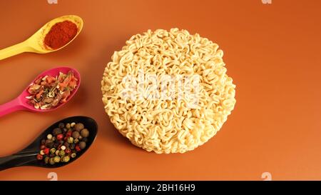 circle of instant noodles with raw spices on a plain brown background. Sprinkle dry Chinese or Korean vermicelli with salt and spices before pouring b Stock Photo