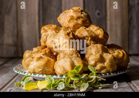 Delicious big cream puffs with cream on aged wooden background. Selective focus. Stock Photo