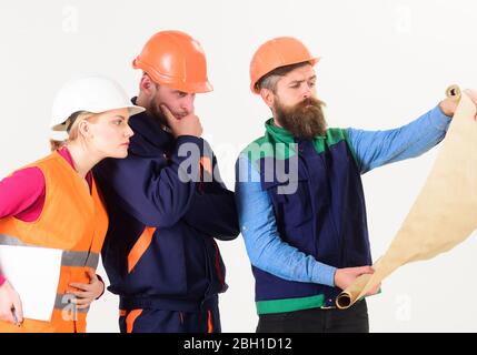 Men and woman in helmets, architects on thoughtful faces looks at drawing, plan, blueprint, project, white background. Team of builder, engineer, architect work on project. Engineering concept. Stock Photo