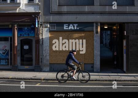 London, UK. 23rd Apr 2020. A lone commuter cycles past a boarded up EAT coffee and food outlet on Fleet Street early this morning in the City of London, as lockdown measures need to be eased out in the next three to four weeks amid coronavirus for the economy to recover. City of London lockdown, England, United Kingdom 23rd April, 2020 Credit: Jeff Gilbert/Alamy Live News Stock Photo