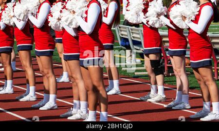 High school cheerleaders in red and white uniforms cheer for the fans at a high school football game. Stock Photo