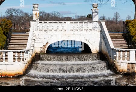 Water flowing over a small waterfall as it runs under a bridge between two lakes at Argyle Park in Babylon New York USA Stock Photo
