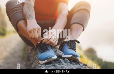 Fit tattoo man tie his sport shoes outdoor during jogging session - Workout and fitness lifestyle concept - Focus on hands Stock Photo