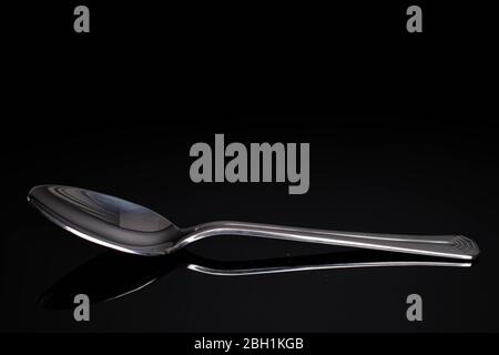 One whole steel silver spoon isolated on black glass Stock Photo