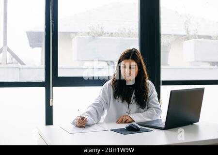 Doctor sitting at desk in medical practice taking notes Stock Photo