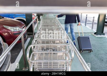 Crop view of man pulling trolley bag walking along row of baggage carts Stock Photo