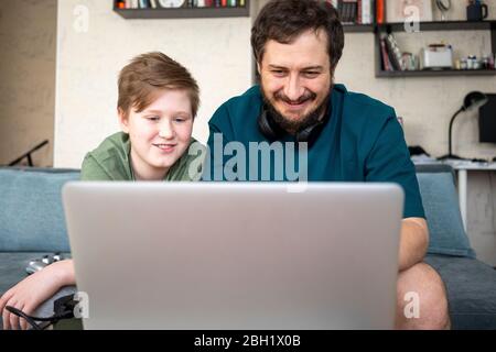 Portrait of father and son sitting together on the couch using laptop Stock Photo