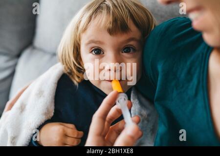 Portrait of sick little girl sitting on couch while mother giving her medication Stock Photo