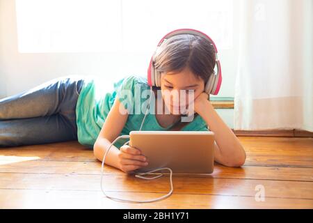 Girl lying on the floor at home using headphones and digital tablet Stock Photo