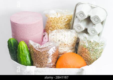 Close up cloth bag with eggs in box, buckwheat, oatmeal, pea, cucumbers, orange, pasta and toilet paper. Home food delivery ordered online on white ba Stock Photo