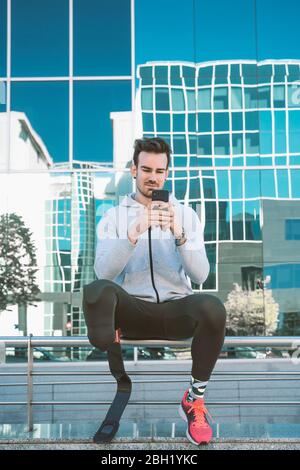 Disabled athlete with leg prosthesis having a break from exercising in the city using cell phone Stock Photo