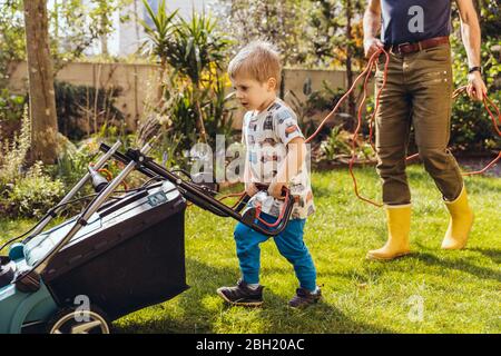 Toddler boy mowing the lawn with his father Stock Photo