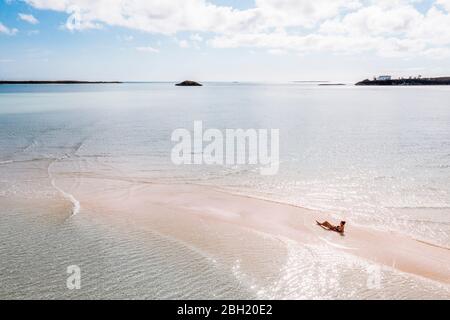 Woman sunbathung on white sand bank in the sea, Bahamas, Carribean Stock Photo