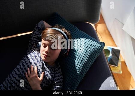 Portrait of boy lying on couch listening music with headphones Stock Photo