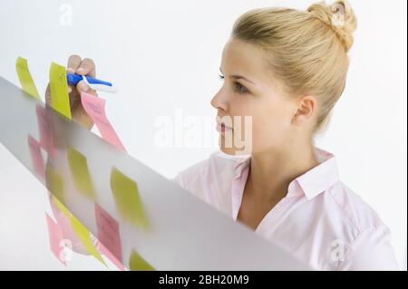 Young businesswoman, standing in office, writing on adhesive notes Stock Photo