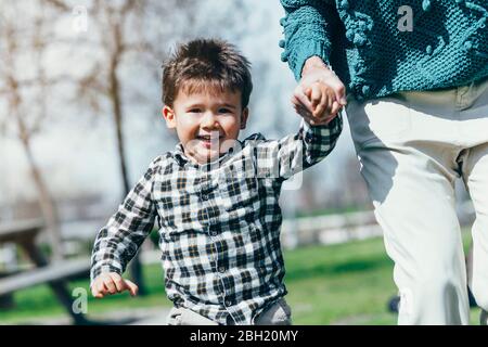 Portrait of happy little boy running hand in hand with his mother in a park Stock Photo