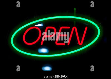 Green ovale neon with another red neon inside shaped into the word Open. Stock Photo