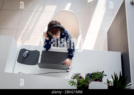 Top view of boy sitting at desk at home wearing headphones and using laptop Stock Photo