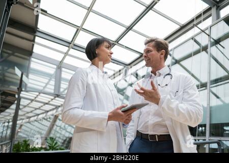 Two doctors standing in atrium, discussing, holding digital tablet Stock Photo