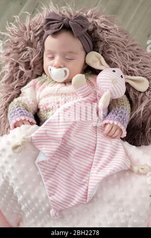 Portrait of sleeping baby girl with hair-band, soft toy and pacifier Stock Photo