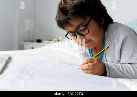 Portrait of little boy lying on bed doing homework Stock Photo