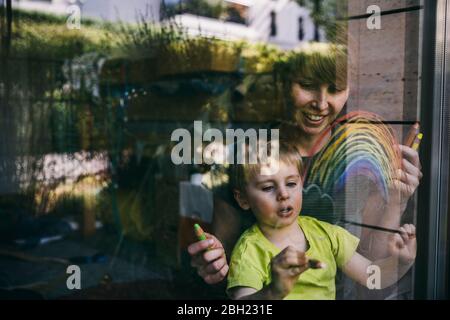 Mother and little son at home drawing rainbow on the window Stock Photo