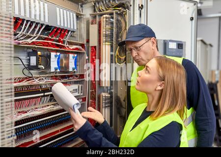 Two electricians with plan looking at fuse box Stock Photo