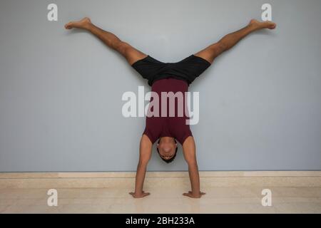 Man doing handstand against the wall at home. Stock Photo