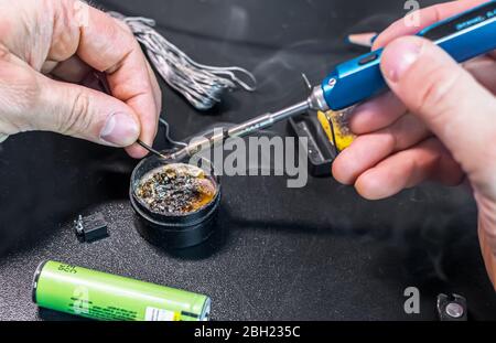 technical master soldering parts with a soldering iron. resin, the smoke, the battery, wires. technical support, repair Stock Photo