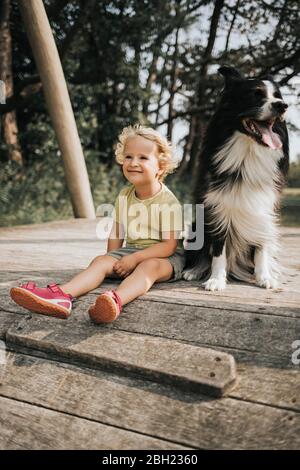 Netherlands, Schiermonnikoog, girl with Border Collie sitting on boardwalk in the forest Stock Photo