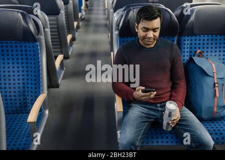 Man holding reusable cup and using smartphone in the train Stock Photo