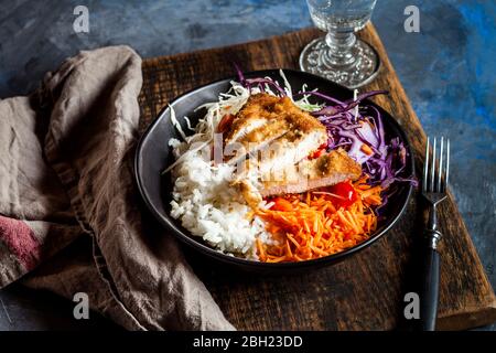 Bowl of ready-to-eat salad with white and red cabbage, carrots, rice and chicken schnitzel Stock Photo