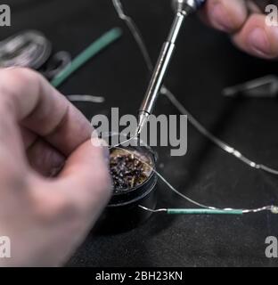 technical master soldering parts with a soldering iron. resin, the smoke, the battery, wires. technical support, repair Stock Photo