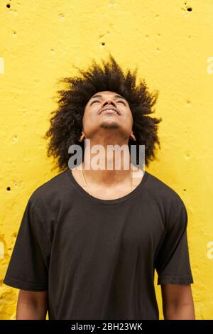 Portrait of young man with afro against yellow wall looking up Stock Photo