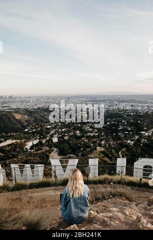 Back view of blond woman sitting behind Hollywood sign looking at view, Beverly Hills, USA Stock Photo