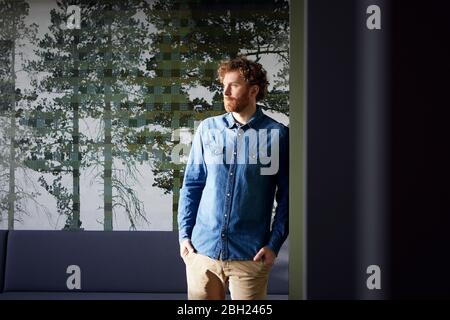 Portrait of a casual businessman standing in front of a wall with picture of trees Stock Photo