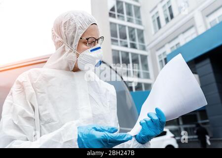 Portrait of tired exhausted female doctor, scientist or nurse wearing face mask and biological hazmat ppe suit reading who treatment protocol or Stock Photo