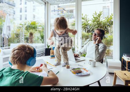 Father talking on the phone while sons are playing on the table Stock Photo