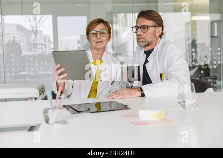 Two doctors sitting at desk using tablet Stock Photo